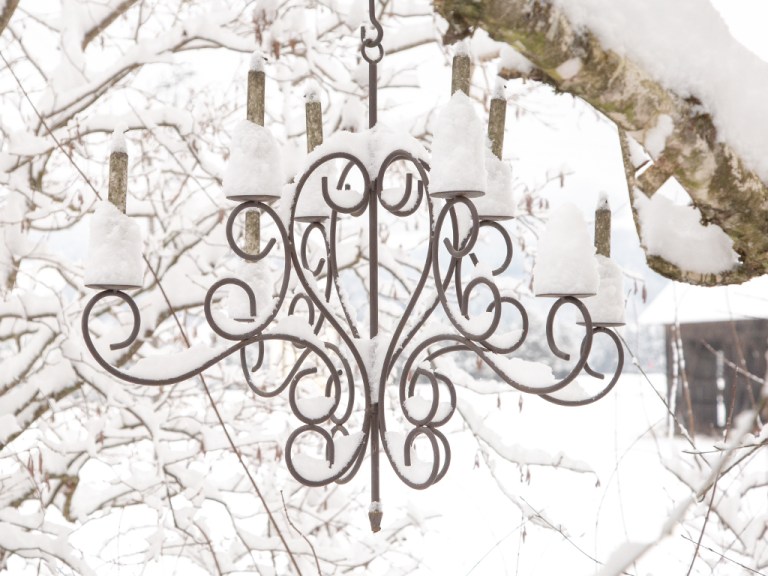 gusseiserne Kerzenlampe, die in der Birke hängt, frisch gefallener Schnee verleiht ihr mit seinen Häubchen einen ganz eigenen Reiz