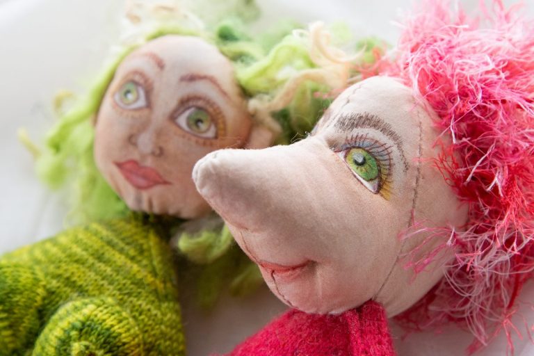 Pinkhaariger Puppenkopf und riesiger Nase und grünen Augen rechts, links grünhaariger Puppenkopf mit grünen Augen, handgemalt, handgenäht und gestrickter Körper, den man angeschnitten sieht