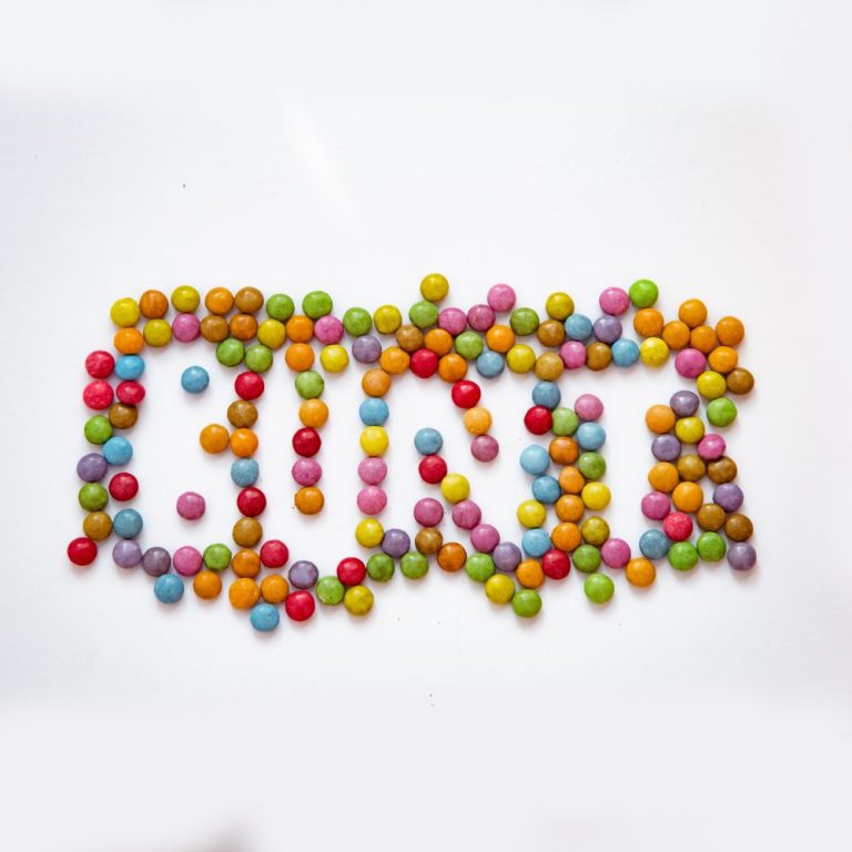viele bunte Smarties, durch Auslassungen entsteht das Wort BUNT auf dem weißen Untergrundpapier