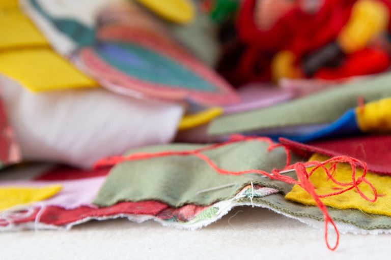 eine Nadel mit rotem Faden durchsticht bunte Filzfarbschichten eines handgenähten Quilts