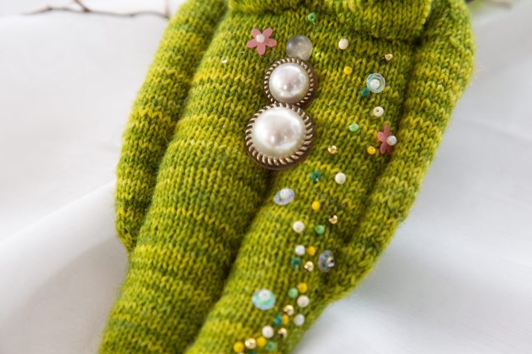 stilisierte Yoni aus Perlmuttknöpfen mit Goldrand, auf gestricktem grünen menschlichem Körper