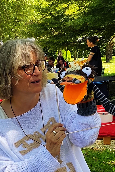 Die Erschafferin einer Klappmaulpuppe aus alten Socken spricht mit ihrem Sockenmonster mit Armen, das ein oranges Maul und riesige Augen hat.